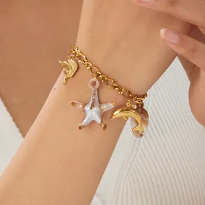 Close-up of gold ocean charm bracelet with starfish and dolphin details on wrist.