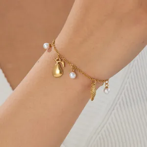 Close-up of a gold-plated charm bracelet with pearls and ocean-inspired elements on a wrist.