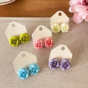 Close-up detail of colorful resin rose stud earrings displayed on white textured cards
