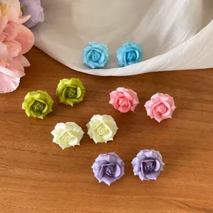 Detail shot of colorful resin rose stud earrings on wooden surface with soft fabric