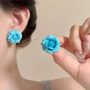 Detailed view of light blue resin rose stud earrings shown on ear and held by hand