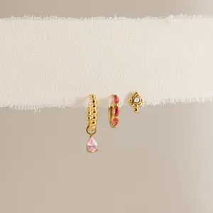 Dettaglio di tre orecchini d'oro con pietre rosa su una fascia di tessuto bianco.