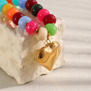 Dettaglio di un ciondolo a cuore dorato su una collana di perle in resina multicolore.