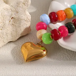 Dettaglio di un ciondolo a cuore dorato su una collana di perle di resina colorate