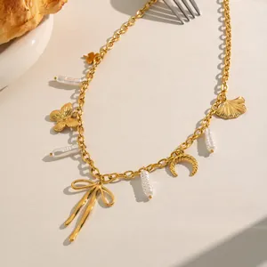 Close-up detail of a gold charm necklace with butterfly, ribbon bow and white pearls