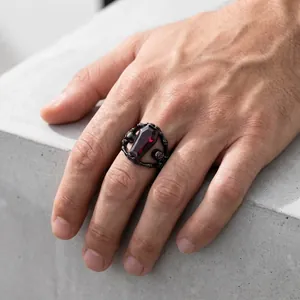Macro view of a gothic coffin-shaped ring featuring a red gem and skeletal hands