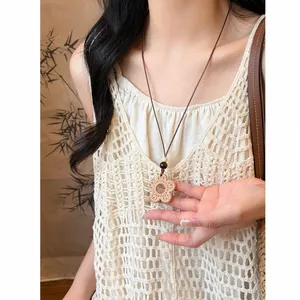 Detailed macro view of bohemian woven flower necklace worn over a white crochet top