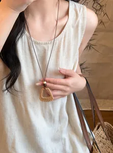Close-up detail of bohemian woven trapezoid pendant necklace worn by model on linen dress