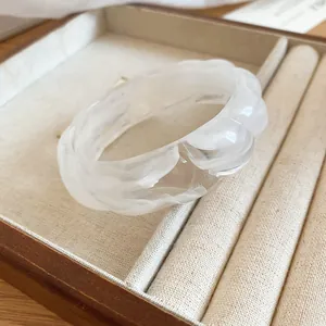 Detail shot of a translucent white marbled acrylic bangle with wavy edges in a jewelry box