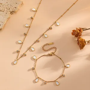 Close-up of gold titanium steel teardrop necklace and bracelet set on warm textured surface.