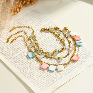 Close-up of stacked gold-plated stainless steel bracelets with colorful acrylic square beads