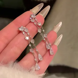 Close-up of sparkling heart and pear-shaped zircon tassel earrings held in hand.