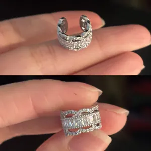 Vue détaillée d'un ear cuff en argent avec zircone, tenu entre les doigts d'une main.