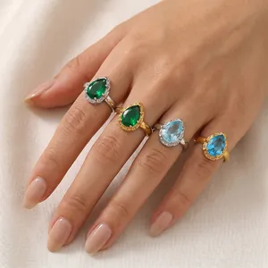 Detalle de elegantes anillos de circón verde y azul en forma de gota en la mano