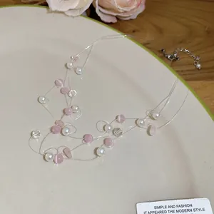 Detail der mehrlagigen Perlenkette mit rosa Perlen auf einem dekorativen Teller.