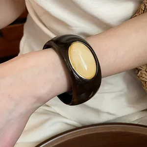Close-up of a wide dark brown acrylic bangle with a marbled cream oval inlay.