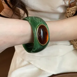Detailed view of a green marble acrylic bangle with an amber oval stone on wrist
