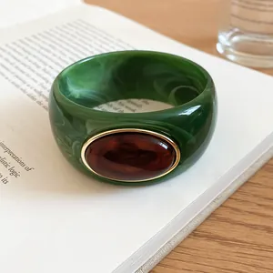 Detail view of a green marbled acrylic bangle featuring a large oval amber resin stone inlay