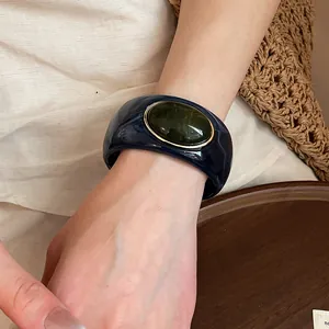 Detail shot of navy acrylic marbled bangle with large green oval stone on model wrist