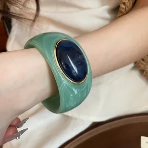 Detail shot of a marbled green and navy blue acrylic chunky bangle on a woman's wrist