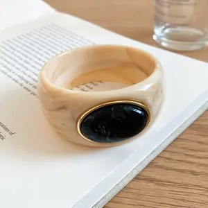 Close-up of acrylic marbled bangle with black oval inlay and gold-tone bezel detail.