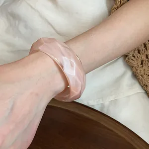 Dettaglio di un bracciale largo in acrilico marmorizzato rosa e bianco con design a onde