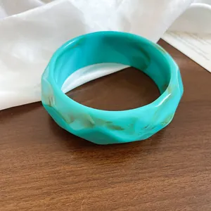 Dettaglio ravvicinato di un ampio bracciale in resina marmorizzata turchese ondulata