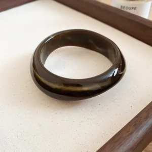 Close-up of an irregular geometric acrylic bangle with deep brown marbled texture and glossy finish