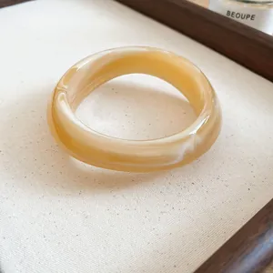 Detail view of irregular acrylic bangle with amber marbleized finish and smooth texture.