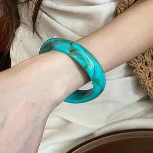 Detailed macro view showing the texture of a green marbled acrylic bangle on wrist.