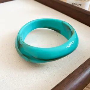 Detailed view of an irregular turquoise acrylic bangle with marbled brown swirls.