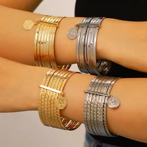 Close-up of multi-layered textured bangles with vintage coin pendants in gold and silver.