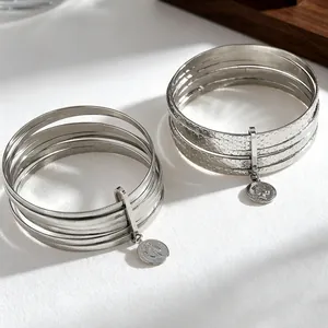Close-up detail of multi-layered silver bangle with hammered texture and coin charm relief