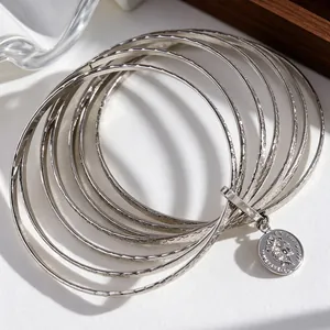 Close-up of multilayered silver bangles featuring hammered texture and vintage coin pendant.