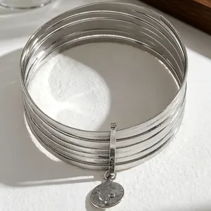 Detailed macro view of silver stacked bangles featuring a vintage coin pendant charm