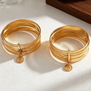 Detailed view of gold multi-layer bangles with frosted texture and vintage coin pendants.
