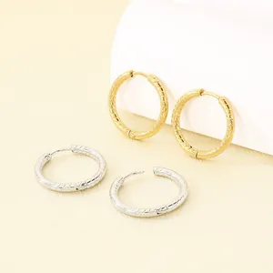Primo piano di orecchini a cerchio in acciaio inossidabile a righe color oro e argento.