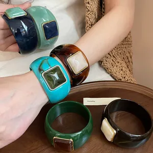 Vista detallada de brazaletes de acrílico con inserciones cuadradas de resina de colores.