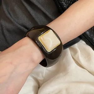 Detalle de una pulsera de acrílico oscuro con una piedra cuadrada de mármol color crema.