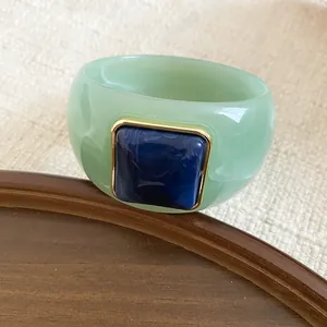 Primer plano de un brazalete de acrílico verde con piedra cuadrada azul oscura incrustada.