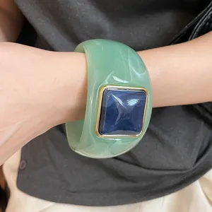 Detalle de un brazalete grueso de acrílico mármol verde con pieza cuadrada azul.