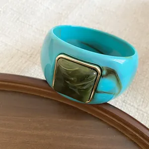 Detalle de brazalete de acrílico azul con elemento cuadrado jaspeado y borde dorado