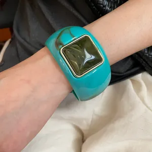 Primer plano detallado de un elegante brazalete de acrílico turquesa con diseño cuadrado