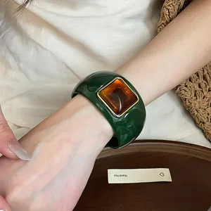 Primer plano de un brazalete de acrílico verde con una piedra central de resina de color ámbar