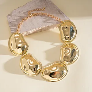 Detailopname van gouden onregelmatige geplooide metalen hangers aan een statement ketting.