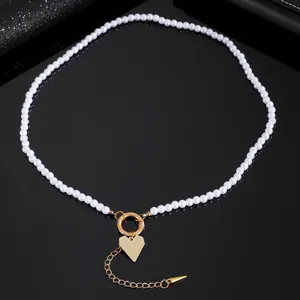 Dettaglio elegante di collana girocollo di perle con ciondolo a cuore dorato e charm a punta.