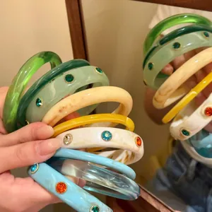 Primo piano di braccialetti in resina colorati con gemme incastonate davanti a uno specchio