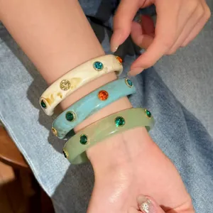 Dettaglio di tre braccialetti rigidi impilabili in acetato con strass colorati sul polso.