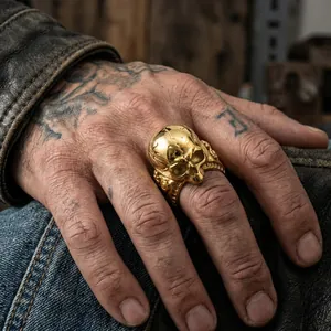 Detail shot of a gold punk skull ring with cracked texture on a tattooed hand.