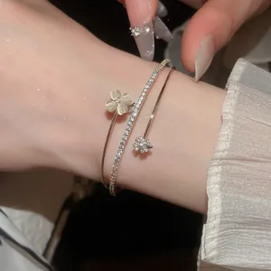 Detailaufnahme eines eleganten zweilagigen offenen Zirkonarmbands mit Kleeblatt-Anhänger.
